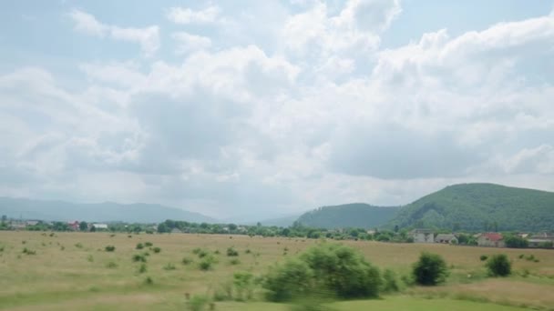 View from window of high-speed train on landscape of beautiful nature wild field and mountains on evening cloudy clean sunny day in summer background. Transport, travel, railway, communication concept — Stock Video