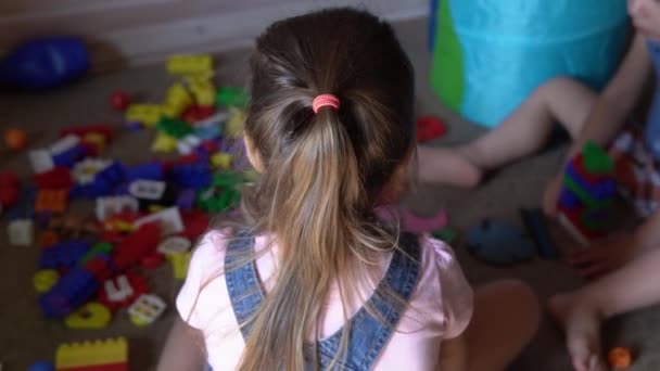 Kleine kleuters en broertjes en zusjes zitten op de vloer met speelgoed in de kinderkamer. De jongens spelen met de bouwvakker in de speelkamer. Kinderen hebben veel plezier thuis gehad. Jeugd, vriendschap, ontwikkelingsconcept — Stockvideo