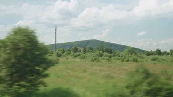 Pohled z okna vysokorychlostního vlaku na krajinu krásné přírody divoké pole a hory les na zataženo čistý slunečný den v letním pozadí. Doprava, cestování, železnice, koncept komunikace — Stock video
