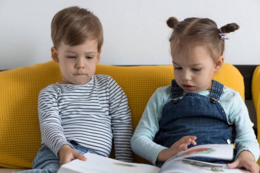 İki küçük çocuk sarı yatakta büyük, ilginç peri masalları kitabı okuyor. Kardeş ikizler evde karantinada eğleniyor, mutlu çocuk. Arkadaşlık, aile, eğitim kavramı