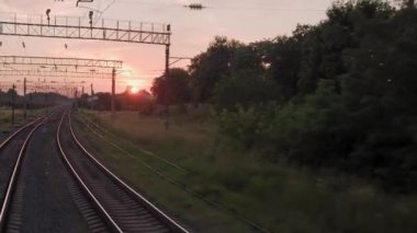 Pencereden yüksek hızlı tren manzarası güzel doğa manzarası vahşi arazi ve orman rayları yaz arkaplanında akşam günbatımında tren rayları. Ulaşım, seyahat, demiryolu, iletişim konsepti
