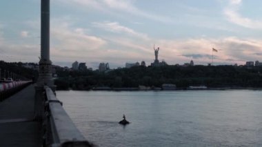 Top Aerial Manzarası, güneş batarken Dnipro nehrinde balıkçıyla birlikte yelkenli sürüyor. Kiev Ukrayna 'daki göller üzerindeki şehir karayolu köprüsündeki manzara trafiği. Su taşımacılığı, seyahat, yaz