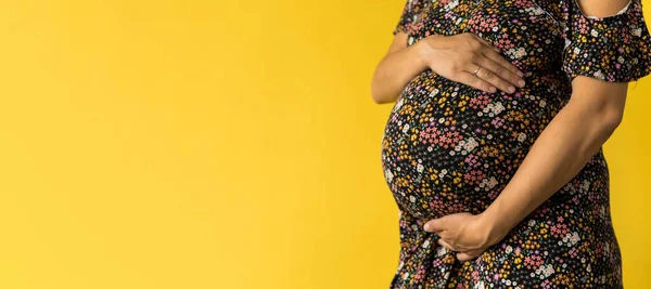 Maternidade, feminilidade, amor, cuidado, espera, verão quente - banner brilhante Close-up mulher grávida irreconhecível em vestido preto floral com as mãos sobre barriga esfregar barriga no fundo amarelo, espaço cópia — Fotografia de Stock