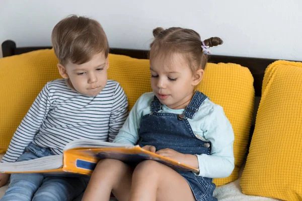 Zwei Vorschul- und Kleinkinder lasen auf gelbem Bett ein großes, interessantes Märchenbuch. Geschwister kleine Zwillinge Leser haben Spaß, glückliches Kind in Quarantäne zu Hause. Freundschaft, Familie, Bildungskonzept — Stockfoto