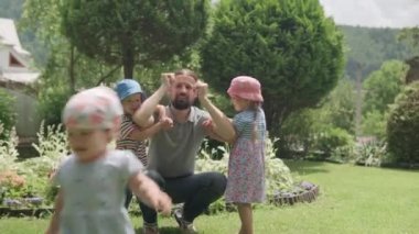 Sakallı ve Kardeşleri Kollarında İki Okul Öncesi Çocuğu Asılı Mutlu Aile Babası. Baba, Kız ve Oğul, Güneşli Yaz Günü 'nde Idyllic Banliyö Evinin arka bahçesinde eğlenceli oyunlar oynuyor.