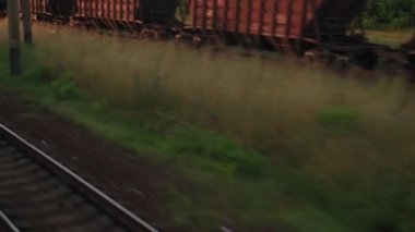 Terk edilmiş eski istasyon ve paslı yük vagonları üzerindeki yüksek hızlı trenden manzara. Tren rayları akşam gökyüzü günbatımında yaz arkaplanında. Ulaşım, seyahat, demiryolu, iletişim konsepti