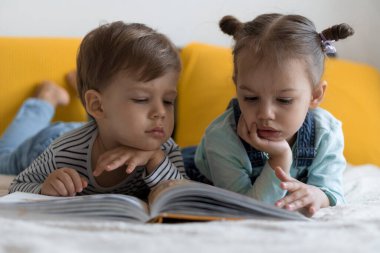 İki küçük çocuk sarı yatakta büyük, ilginç peri masalları kitabı okuyor. Kardeş ikizler evde karantinada eğleniyor, mutlu çocuk. Arkadaşlık, aile, eğitim kavramı