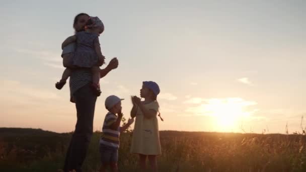 Menschen im Park. glückliche Familie lächelt applaudiert. Papa mit vielen Kindern auf einem Berg im hohen Gras vor Sonnenuntergang. Eltern und lustige Kinder schauen in die Ferne. Sommer, Vaterschaft, Kindheitskonzept — Stockvideo