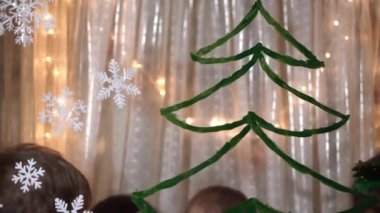 Otantik sevimli bir anne ve iki küçük anaokulu öğrencisi kız ve erkek kardeş 2-4 yaşlarında pencereye Noel ağacı çiziyor. Çocuklu genç bir kadın kar taneleri yapıştırıyor. Xmas, yeni yıl, kış konsepti.