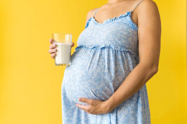 Retrato recortado bonito mulher grávida irreconhecível em vestido azul floral segurar beber copo de leite no espaço cópia fundo amarelo. Maternidade, feminilidade, alimentação saudável, laticínios, conceito de verão quente — Fotografia de Stock
