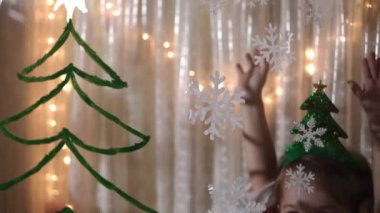 Otantik sevimli bir anne ve iki küçük anaokulu öğrencisi kız ve erkek kardeş 2-4 yaşlarında pencereye Noel ağacı çiziyor. Çocuklu genç bir kadın kar taneleri yapıştırıyor. Xmas, yeni yıl, kış konsepti.