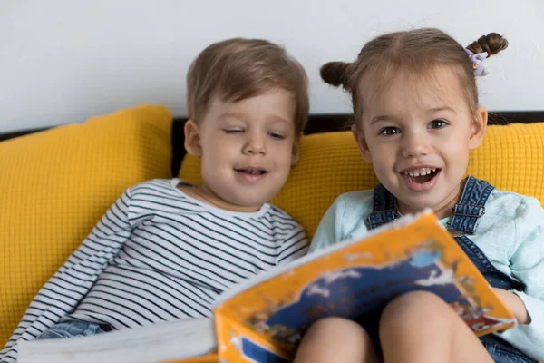 Zwei Vorschul- und Kleinkinder lasen auf gelbem Bett ein großes, interessantes Märchenbuch. Geschwister kleine Zwillinge Leser haben Spaß, glückliches Kind in Quarantäne zu Hause. Freundschaft, Familie, Bildungskonzept — Stockfoto