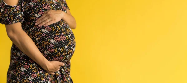 Maternidade, feminilidade, amor, cuidado, espera, verão quente - banner brilhante Close-up mulher grávida irreconhecível em vestido preto floral com as mãos sobre barriga esfregar barriga no fundo amarelo, espaço cópia — Fotografia de Stock