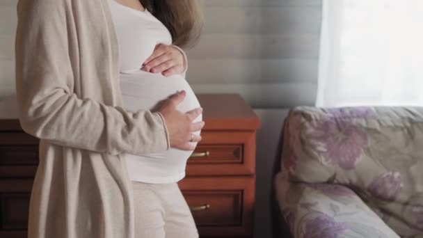 Primo piano di donna incinta senza volto che tocca pancia a casa vicino alla finestra. la madre premurosa accarezza la grande pancia nuda con le mani, sulla stanza di provenienza leggera. gravidanza, maternità, persone, concetto di aspettativa — Video Stock