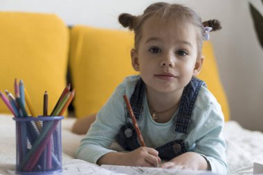 Zeki, gülümseyen, küçük bir çocuk çocuk ve kız sarı yatakta göbeklerinde kalemlerle resim yapıyorlar. Küçük sevimli okuyucu evde karantinada eğleniyor, mutlu çocuk. Arkadaşlık, aile, eğitim.