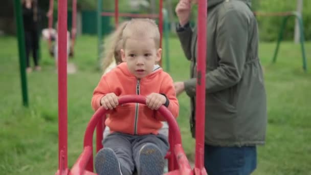 Bonito crianças pré-escolares bonitas com a jovem mãe brincadeira no trem swing no parque infantil. Pequeno bebê rindo divirta-se, balançando no bordo de balancé jogando. Conceito de infância feliz, emoções positivas, POV — Vídeo de Stock