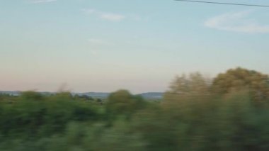 Yüksek hızlı trenin penceresinden manzarası güzel doğa manzarası vahşi arazi ve orman akşam bulutlu gökyüzü günbatımı yaz arkaplanında. Ulaşım, seyahat, demiryolu, iletişim konsepti