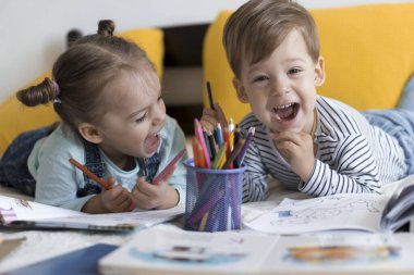 Zeki, gülümseyen, küçük bir çocuk çocuk ve kız sarı yatakta göbeklerinde kalemlerle resim yapıyorlar. Küçük sevimli okuyucu evde karantinada eğleniyor, mutlu çocuk. Arkadaşlık, aile, eğitim.