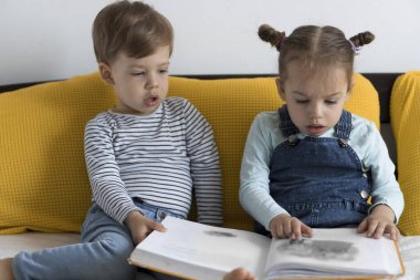 İki küçük çocuk sarı yatakta büyük, ilginç peri masalları kitabı okuyor. Kardeş ikizler evde karantinada eğleniyor, mutlu çocuk. Arkadaşlık, aile, eğitim kavramı