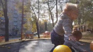 Sonbahar, spor, bayram, aile, çocukluk - iki mutlu küçük kardeş kardeş ikiz çocuklar trambolinde eğlenceli zıplama topları oynuyorlar güneşli bir akşam günbatımında parkta..