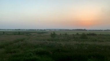 Güzel doğa manzarası, vahşi tarlalar ve dağların ormanı üzerinde yaz arkaplanındaki açık güneşli akşam günbatımında yüksek hızda dönen trenin mavi kenar görüntüsü. Ulaşım, seyahat, demiryolu kavramı