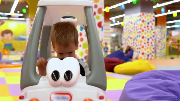 真正快乐可爱的小幼儿园男孩开车在游戏室。孩子们在儿童娱乐中心呆在一起。宝宝在操场上玩的开心。童年、发展、休闲概念 — 图库视频影像