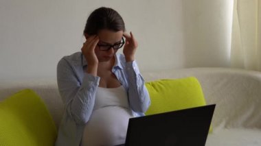 Stresli, stresli iş kadını hamile ve dizüstü bilgisayarı koltukta dinleniyor. Depresyondaki Ledy Hamilelik Çalışması Uzaktan Akıllı Telefon İnternet Çevrimiçi Teknolojisini Evde Kullanıyor. Annelik izni kavramı