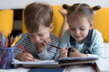 Zeki, gülümseyen, küçük bir çocuk çocuk ve kız sarı yatakta göbeklerinde kalemlerle resim yapıyorlar. Küçük sevimli okuyucu evde karantinada eğleniyor, mutlu çocuk. Arkadaşlık, aile, eğitim.