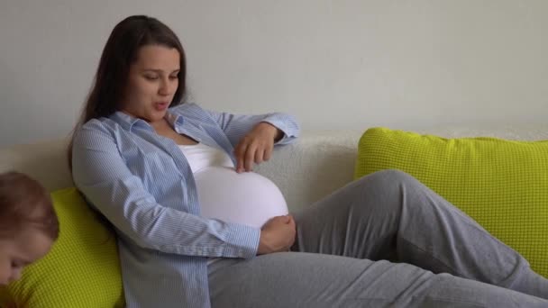 Femme enceinte mignonne caresse gros ventre toucher le ventre dans la journée ensoleillée. Jeune Ledy pendant la grossesse amusez-vous passer du temps sur le canapé jaune à la maison. Maternité, paternité, médecine Santé et soins prénatals — Video