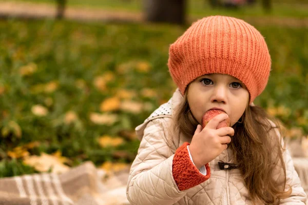 Close Up Portret van kleine schattige kleuter meisje in oranje baret op gele gevallen bladeren eet rode appel kijken naar camera koud weer in het najaar Park. Jeugd, Familie, Moederschap, Herfst Concept — Stockfoto
