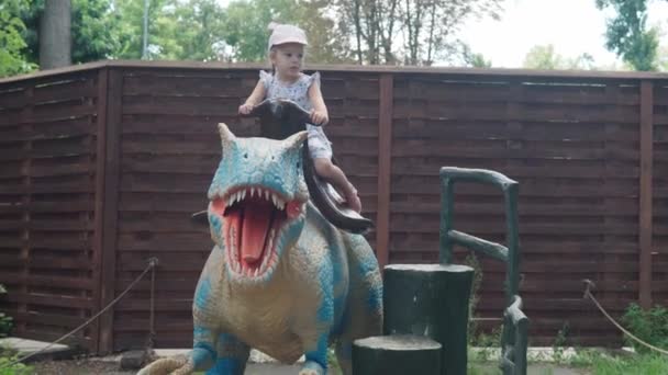 2021.08.12 - Kyjev, Ukrajina: Dívka sedí na motorizovaném dinosaurovi Predátor Dragon Mockup v zábavním parku. Výstava pohyblivých modelů Zvířata z prehistorického období v Dinoparku — Stock video