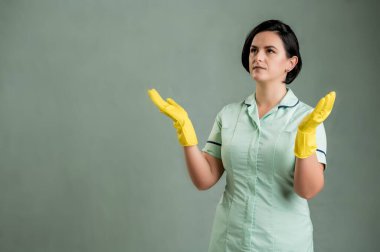 Yeşil tişörtlü ve sarı eldivenli genç temizlikçi kadın, kolları açık, yukarı bakıyor, yeşil arka planda yalıtılmış kenar manzaralı