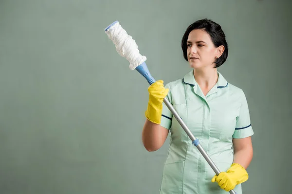年轻的清洁女工穿着绿色衬衫和黄色手套 拿着绿色背景的拖把 图库图片