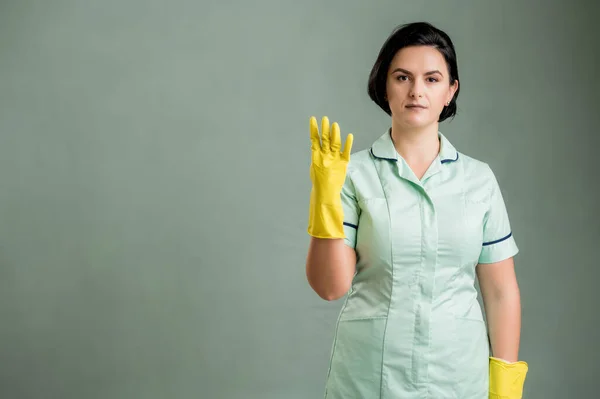 年轻的清洁女工穿着绿色的衬衫和黄色的手套 手指被绿色的背景隔开 数着四个 免版税图库照片