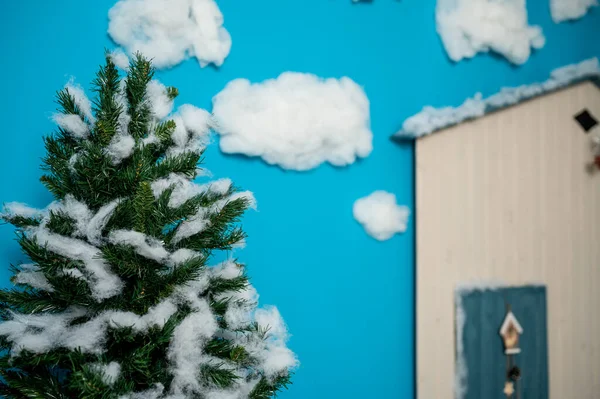 装饰圣诞工作室 带有蓝色门 木制长椅和滑雪板 假云彩和雪的房子 图库照片