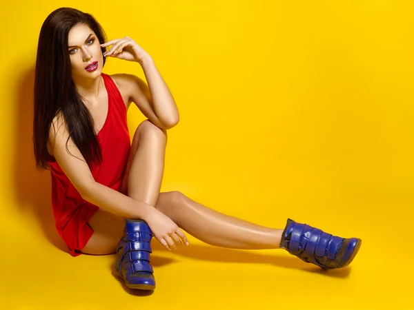 Gyönyörű fiatal lány pózol, piros póló, szép és egészséges haj, sárga háttér, kék cipők — Stock Fotó