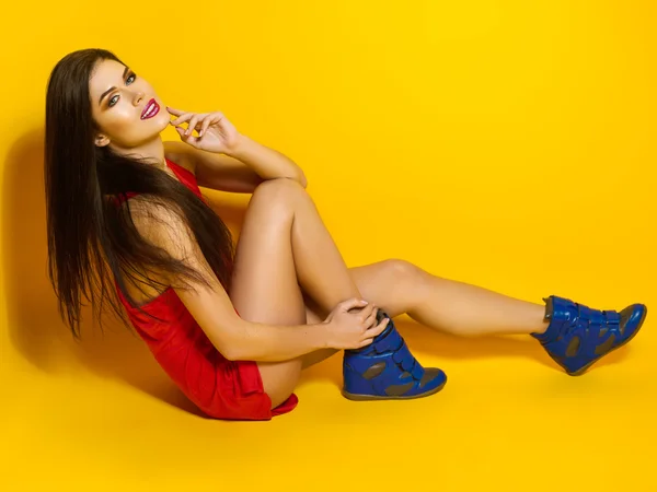 Mooi jong meisje glimlachend en poseren voor een foto, een rood T-shirt, mooi en gezond haar, gele achtergrond, blauwe sneakers — Stockfoto