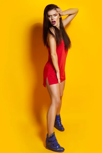Belle jeune fille posant pour une photo, un T-shirt rouge, beaux cheveux sains, fond jaune, baskets bleues — Photo