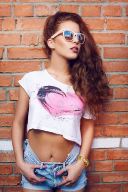 Bir tuğla duvar bir arka plan üzerinde güneş gözlüğü güzel genç kız. Güzel sağlıklı saçlar. Kot şort