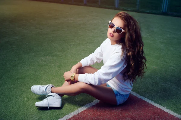 Beautiful young girl in sunglasses on the tennis court. Beautiful healthy hair. Denim shorts. White sneakers — Stock Photo, Image