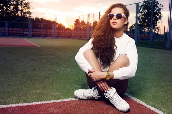 Beautiful young girl in sunglasses on the tennis court. Beautiful healthy hair. Denim shorts. White sneakers — Stock Photo, Image