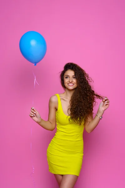 Hermosa y joven chica en un vestido amarillo sosteniendo un globo azul y sonriendo sobre un fondo rosa —  Fotos de Stock