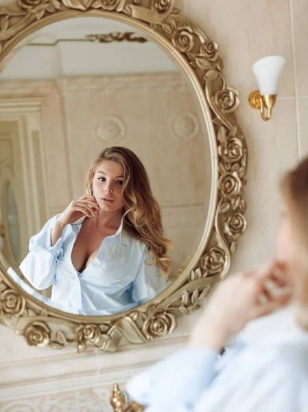 Beautiful young sexy girl in a shirt is looking at herself in the bathroom mirror — Stock Photo, Image