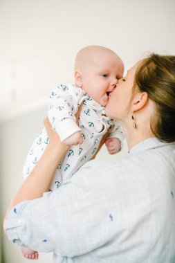 Genç anne kollarını tutuyor ve küçük oğlunu evinde öpüyor. Annem mutlu. Çocuk mutlu ve gülüyor. Aile kavramı.
