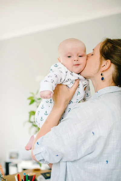 Mladá matka se drží v náručí a líbá svého malého syna doma. Máma šťastná. Dítě šťastné a smějící se. Koncept rodiny — Stock fotografie