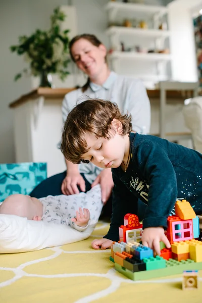 Niño jugando en el constructor en el suelo de la casa. Mi madre lo está vigilando. El concepto de familia — Foto de Stock