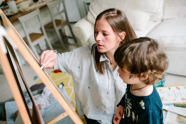 La jeune mère dessine une craie sur un tableau noir avec son jeune fils. Le concept de famille — Photo