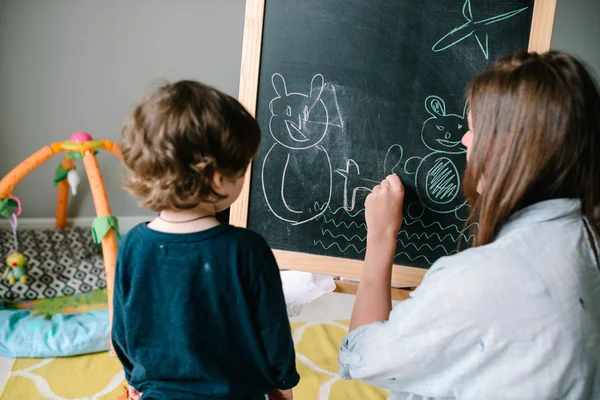 Mladá matka kreslí křídu na tabuli se svým malým synem. Koncept rodiny — Stock fotografie