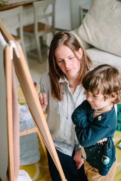 La jeune mère dessine une craie sur un tableau noir avec son jeune fils. Le concept de famille — Photo