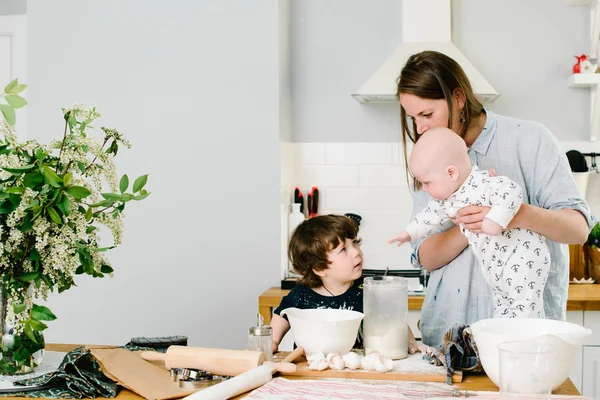 Young and happy mom with her children in the kitchen cook cookie